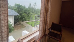 Un balcón con vistas a un jardín y un edificio. Hay dos sillas de madera y una mesa de vidrio.