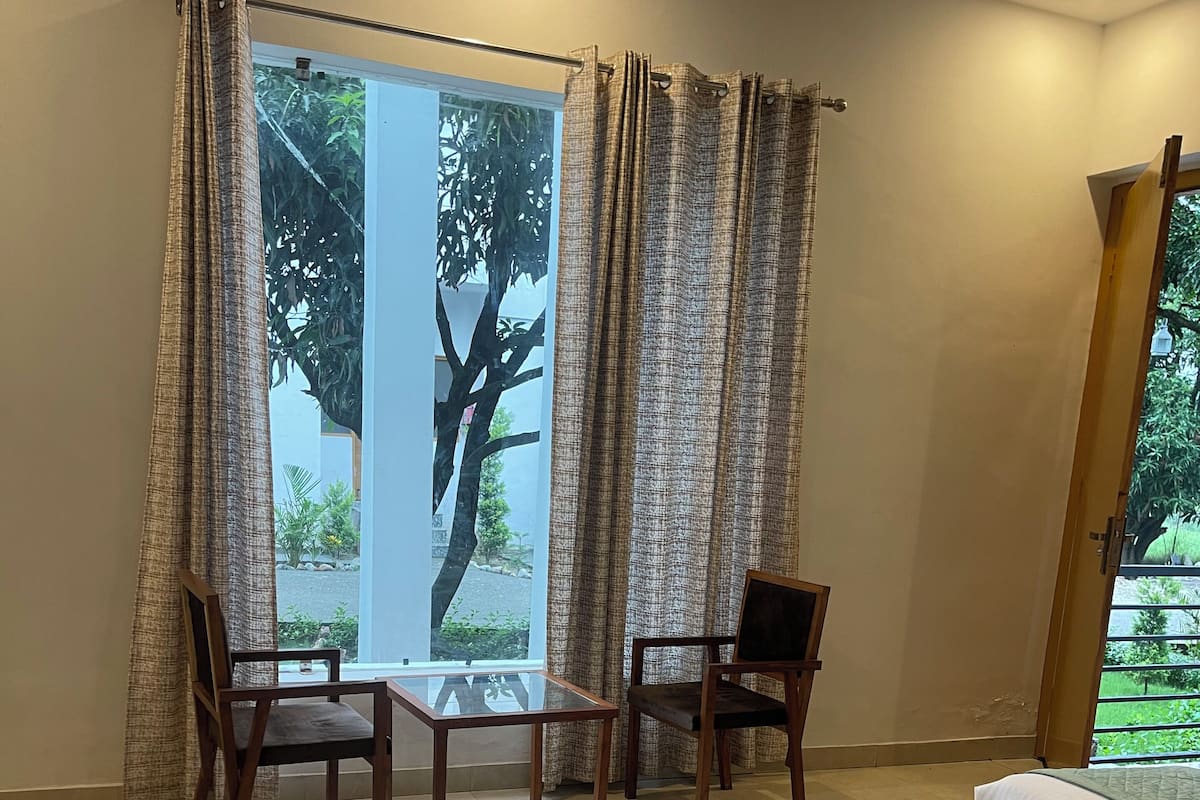A bedroom with a bed, two chairs, a table, and a large window with curtains.