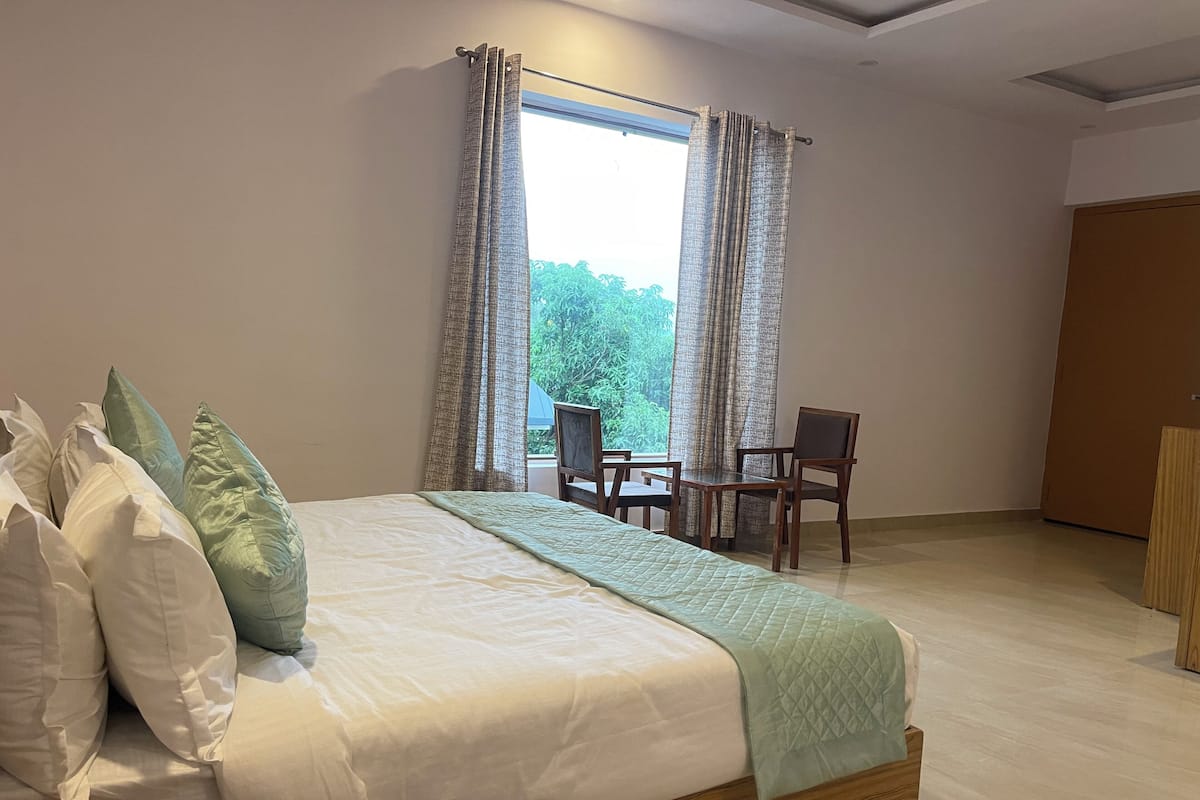 A bedroom with a large bed, a bedside table, a chair, and a window with curtains.