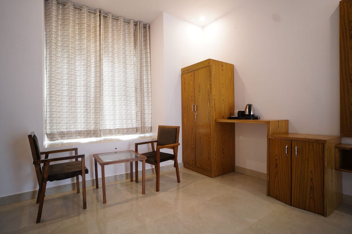 A room with a wooden wardrobe, a small table, two chairs, and a window with curtains.