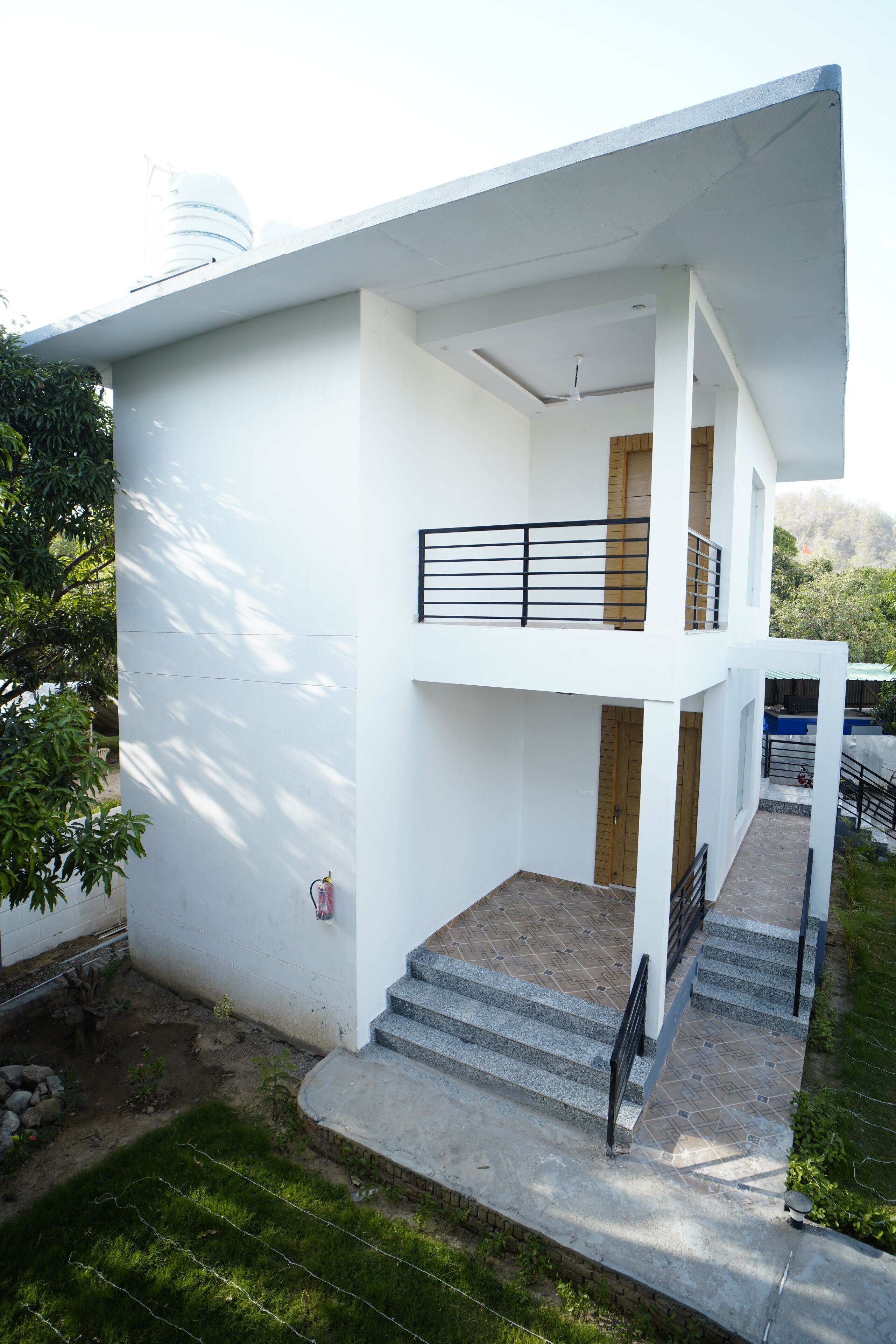 Een modern huis met twee verdiepingen, een balkon, een trap en een kleine tuin.