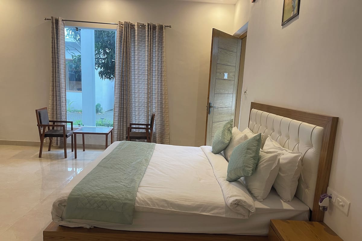 A bedroom with a bed, bedside table, and a chair near a window with curtains.