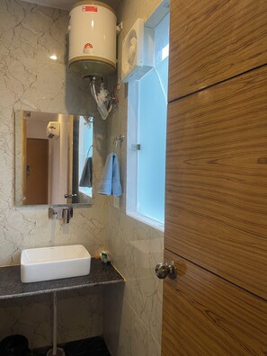 A bathroom with a marble wall, a white sink, a towel rack, and a wooden door. - THE WHITE OAK CORBETT SPA & RESORT (Ramnagar)
