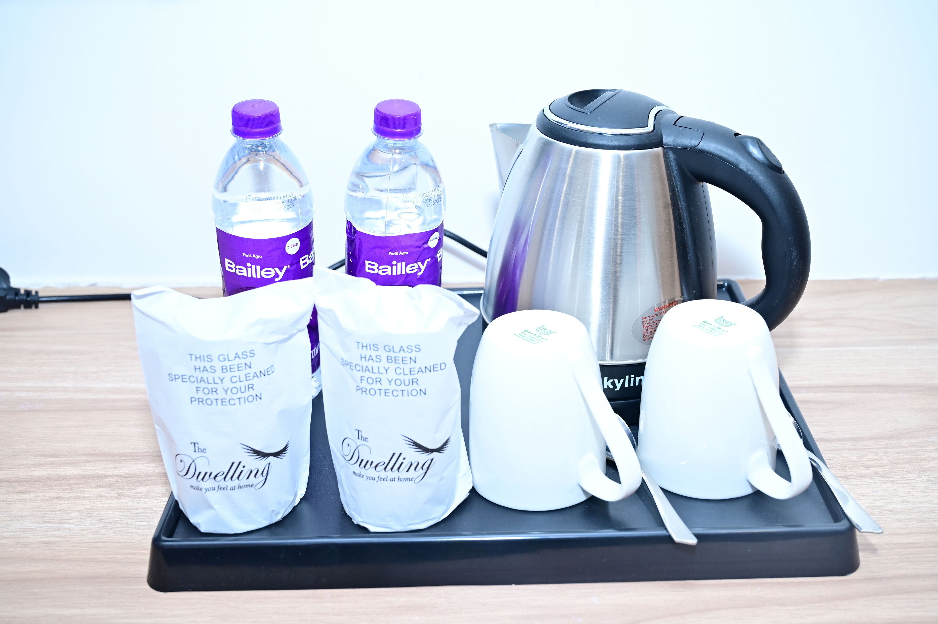Een dienblad met Bailey waterflessen, een waterkoker en twee glazen zakken met de tekst 'The Dwelling'.