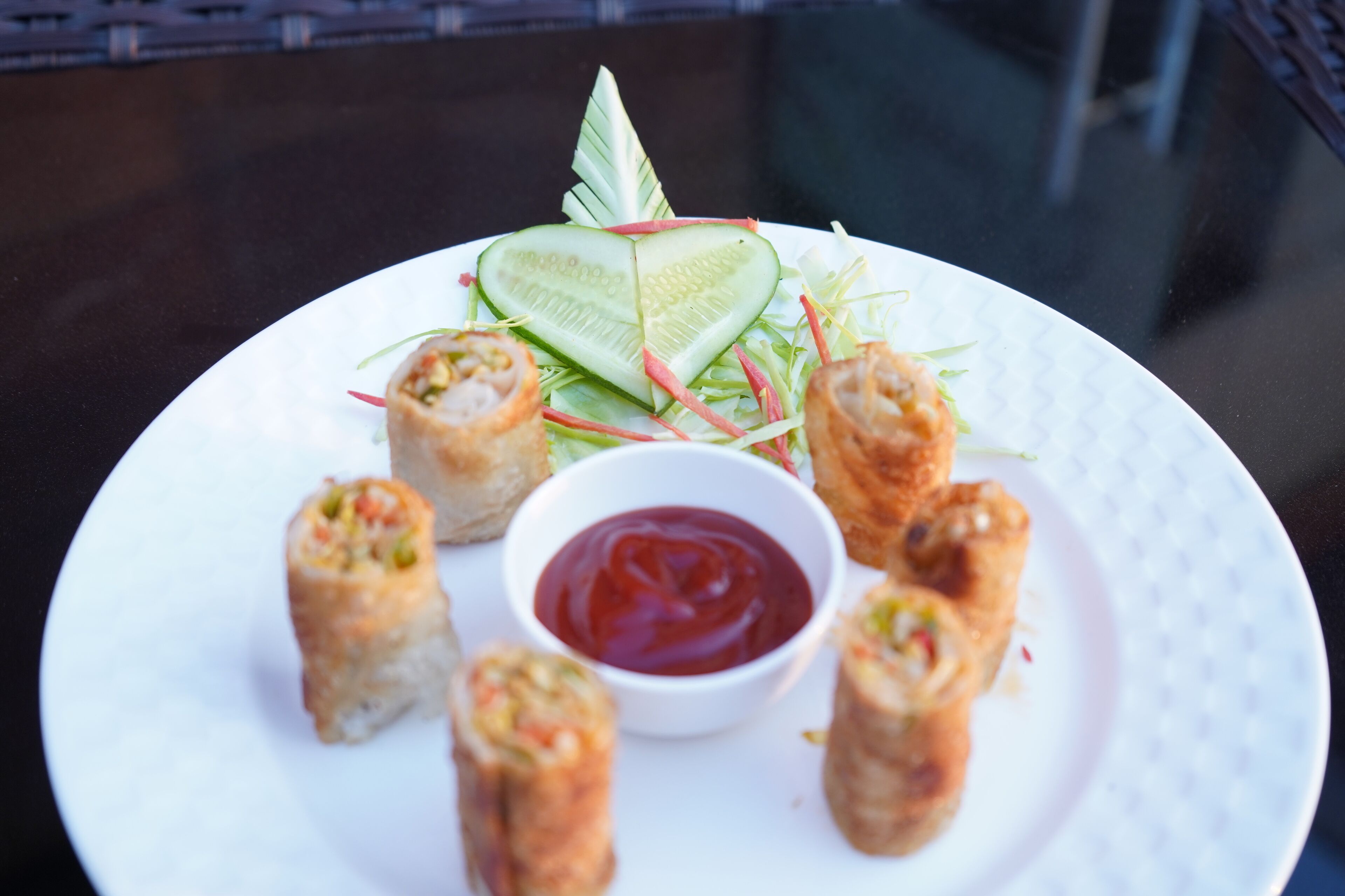 Un plato de rollitos de primavera con kétchup y rodajas de pepino.