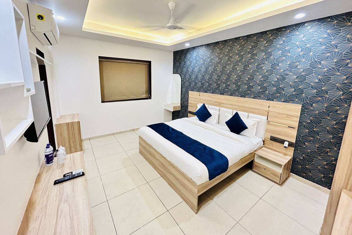 A modern hotel room with a wooden bed, bedside tables, a ceiling fan, a window with a blind, and a wall with a geometric pattern.