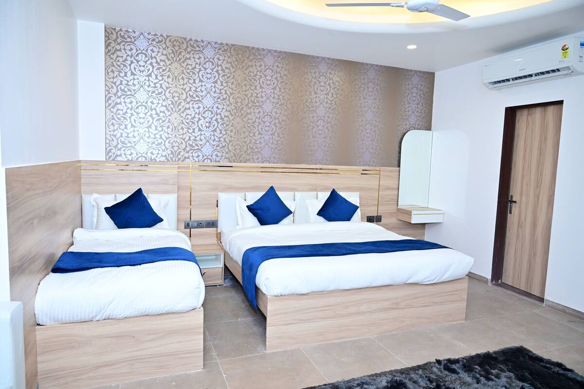A modern hotel room with two beds, a ceiling fan, an air conditioning unit, and a patterned wallpaper.