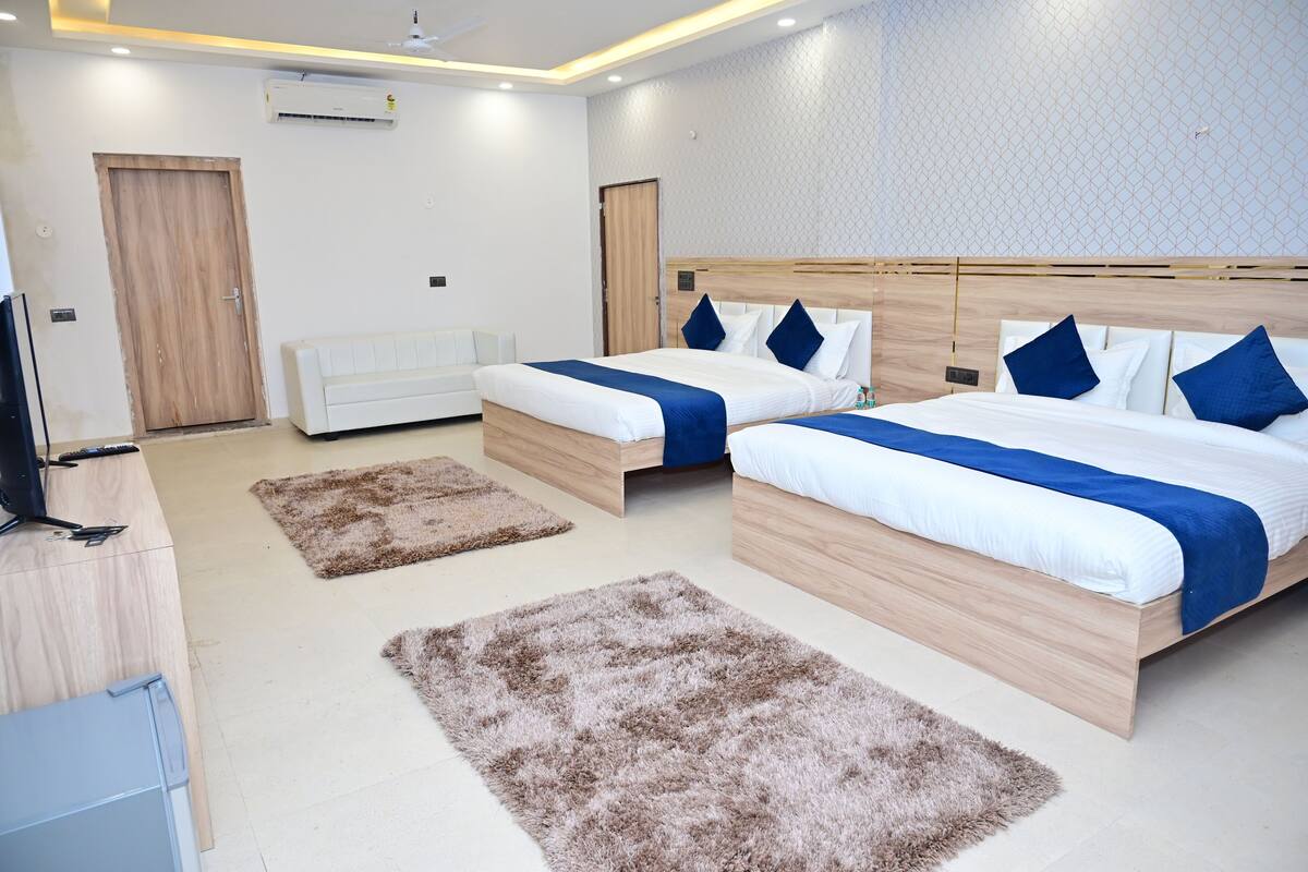 A modern hotel room with two beds, a sofa, and a TV.