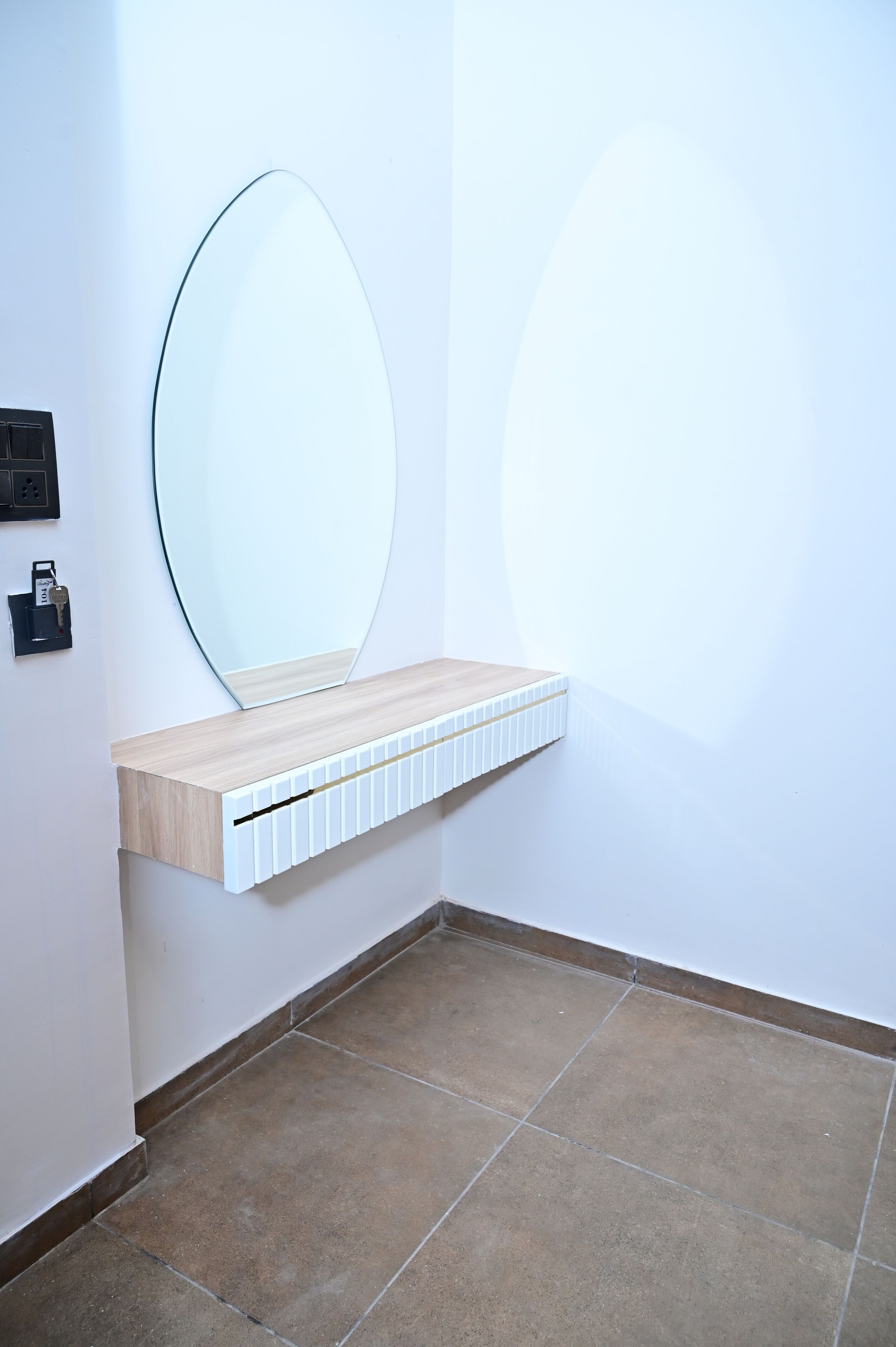 A corner bathroom with a wooden vanity, a large mirror, and a wall-mounted light switch.