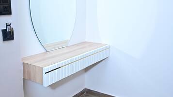 A corner bathroom with a wooden vanity, a large mirror, and a wall-mounted light switch.