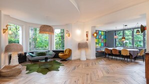A spacious living area with a herringbone floor, a sofa, a dining table with chairs, and large windows with a view of greenery. - La clarté - wonderful refurbish home with garden and pool (Champagne-au-Mont-d'Or)