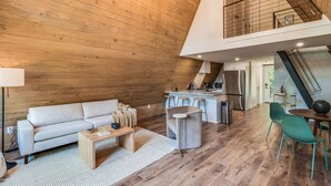 Ein modernes Loft mit Holzvertäfelung, einer Küche mit großer Kochinsel und einem Essbereich mit grünen Stühlen.