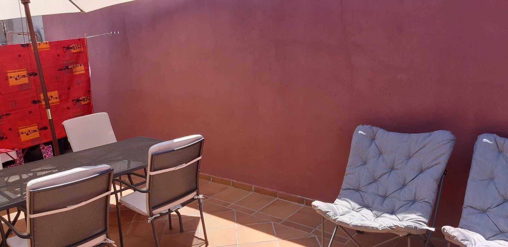 Een terras met een tafel en stoelen, een rode muur en een betegelde vloer.