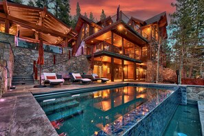 A large, multi-level wooden cabin with a swimming pool, stone walls, and outdoor seating.