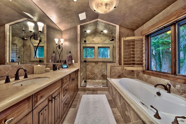 A spacious bathroom with a large bathtub, two sinks, a walk-in shower, and a large mirror.