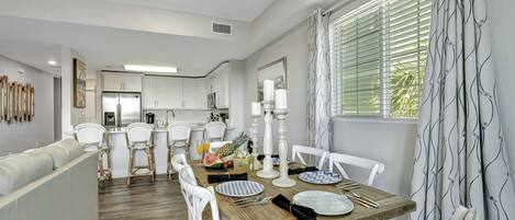 A modern kitchen with white cabinetry and a dining area with a wooden table set for four.