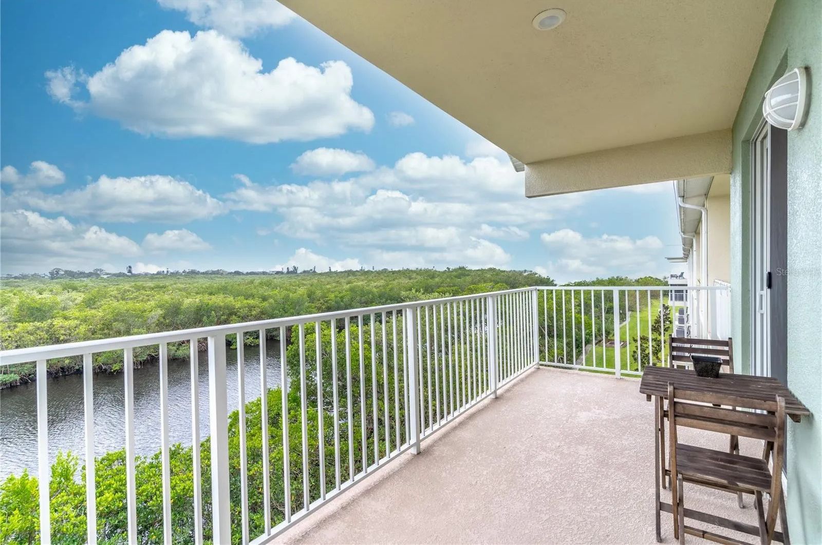 A balcony with a view of a river and greenery, a white railing, and a table with chairs.