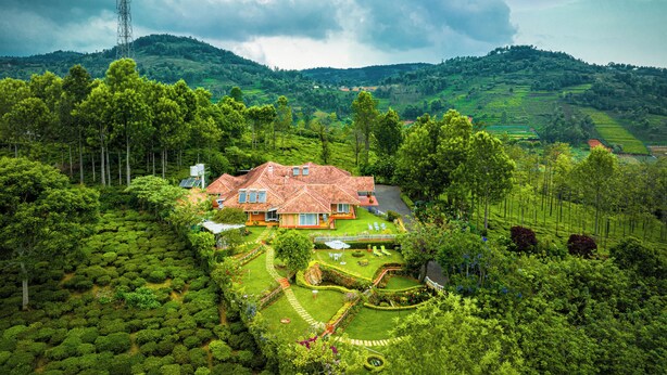 A house with a red roof surrounded by lush greenery and a hill in the background.