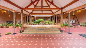 A covered patio area with a tiled floor, potted plants, and a wooden ceiling structure.