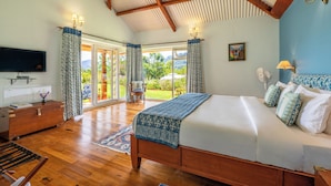 A spacious bedroom with a large bed, wooden floor, and a view through glass doors to a garden.