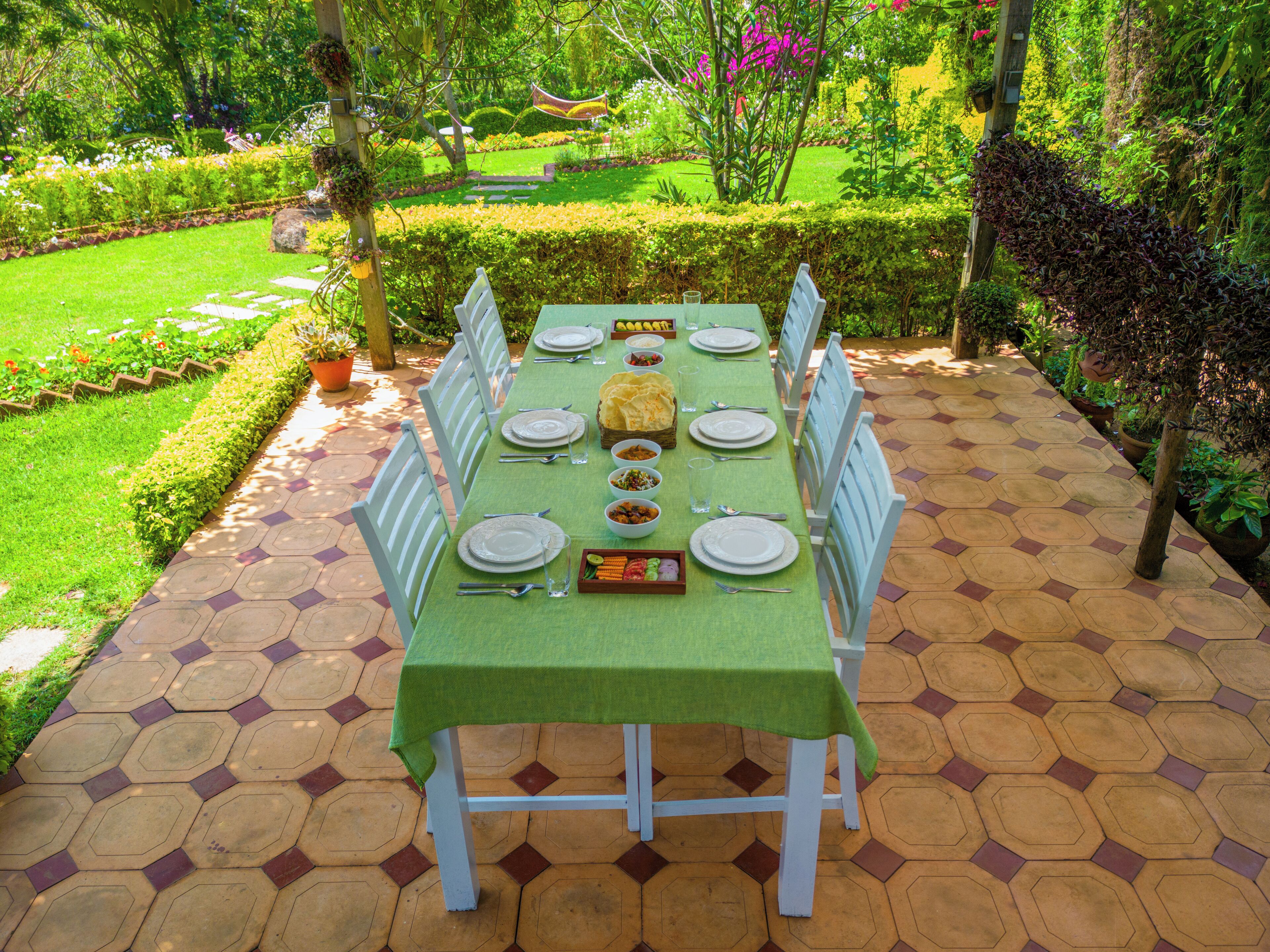 Mesa de comedor al aire libre con mantel verde, sillas blancas y una variedad de platos.