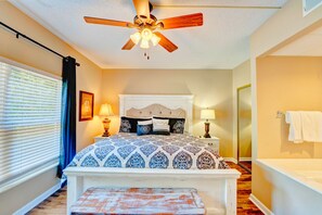 A bedroom with a bed, bedside lamps, a ceiling fan, and a window with blinds.