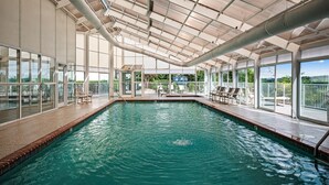 Ein Innenpool mit großen Glaswänden, Fliesenboden und einer Decke mit freiliegenden Rohren.