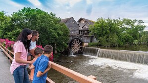 Eine Familie steht neben einem Wasserspiel mit einer großen Radkonstruktion im Hintergrund.