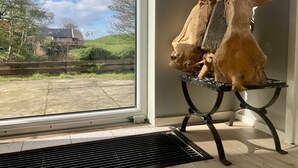 A room with a large window, a wooden sculpture on a stand, and a view of a green landscape.