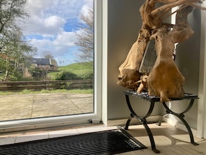 A room with a large window, a wooden sculpture on a stand, and a view of a green landscape.