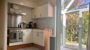 A modern kitchen with stainless steel appliances, wooden cabinets, and a large window offering a view of trees.