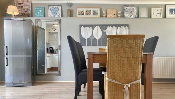 A dining area with a wicker chair, a table, and a refrigerator.