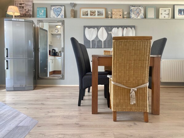 A dining area with a wicker chair, a table, and a refrigerator.