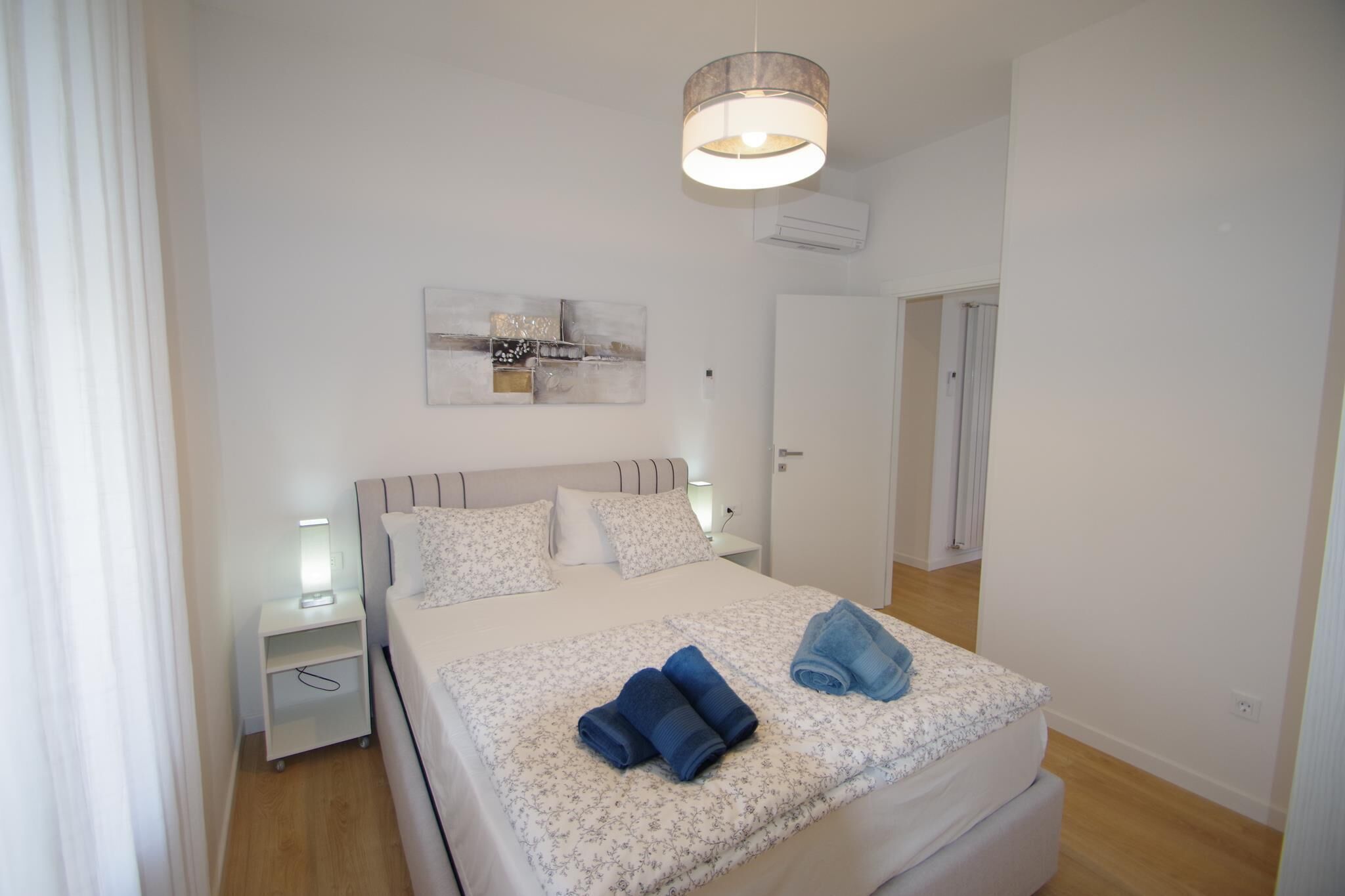 Um quarto moderno com uma cama, mesas de cabeceira, uma obra de arte na parede e um lustre.