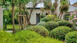 Un jardín con diversas plantas y árboles, un edificio pequeño con una puerta y un muro.
