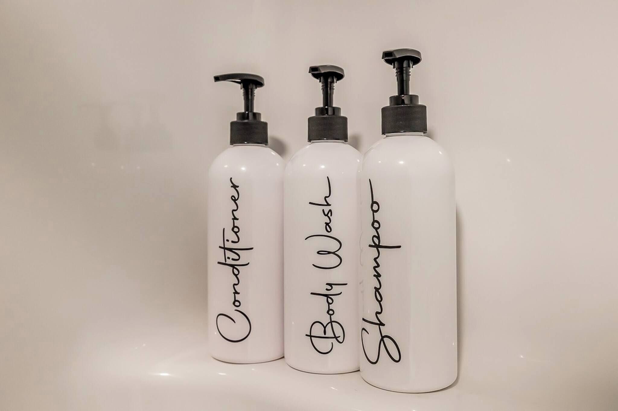 Tre flaconi di prodotti per la cura personale con l'etichetta 'Conditioner', 'Detergente corpo' e 'Shampoo'.