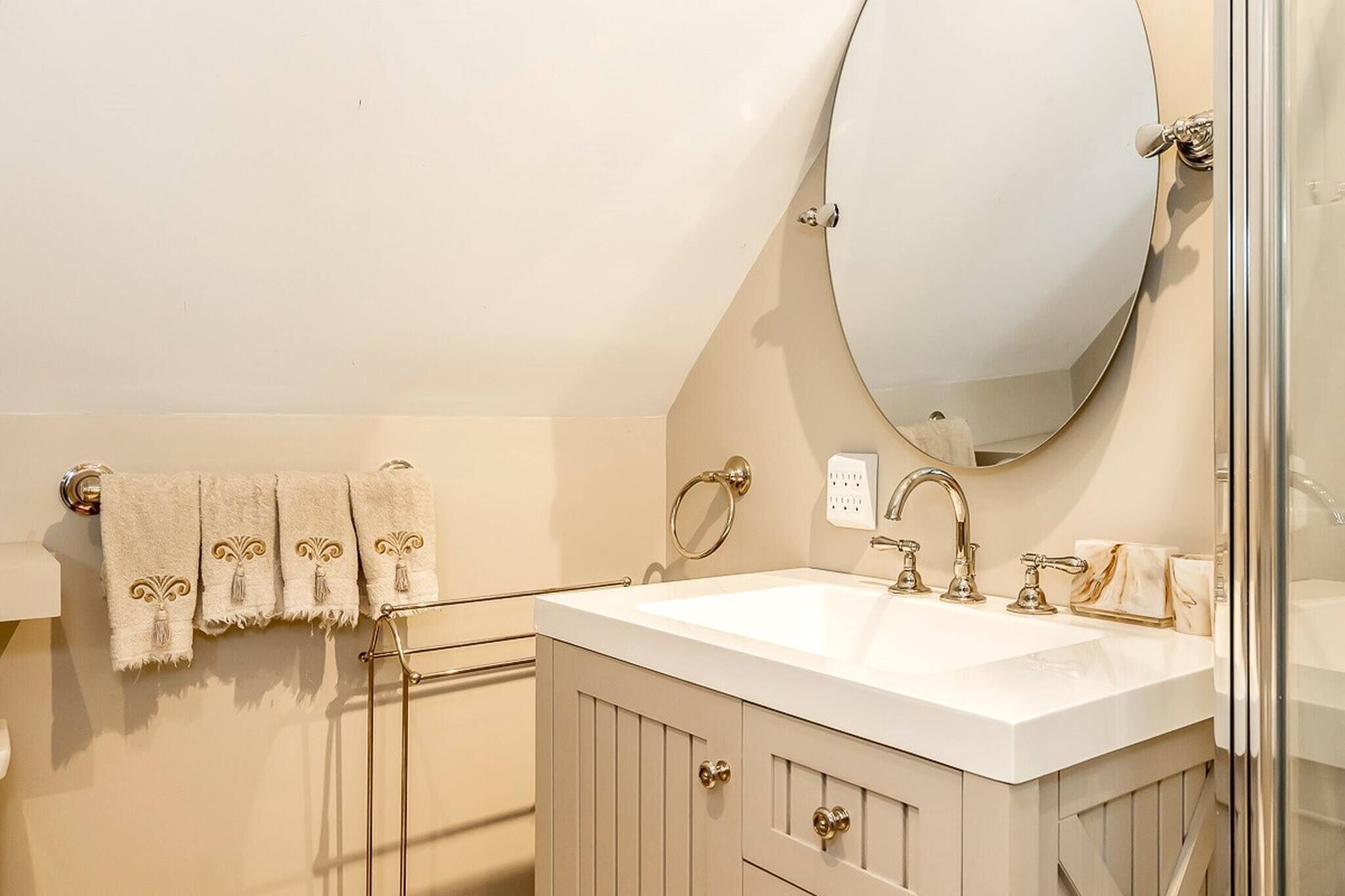 A bathroom with a white sink, a large mirror, and a towel rack with three towels.
