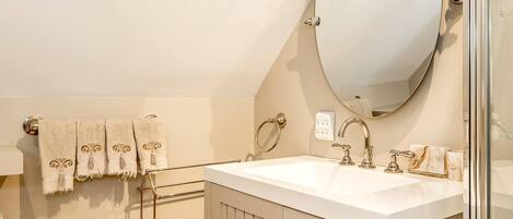 A bathroom with a white sink, a large mirror, and a towel rack with three towels.