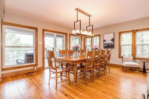 A dining area with a wooden table and chairs, large windows, and a hanging light fixture. - Muskoka Lakeshore Cottage Bliss (Gravenhurst)