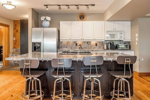 Una cocina moderna con una isla central, taburetes de bar, armarios blancos y un reloj en la pared.
