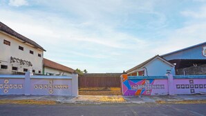 Une entrée fermée par un portail en métal, un mur aux couleurs vives orné de motifs géométriques et un bâtiment doté d’un toit en pente.
