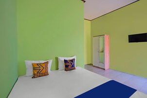 Una habitación con una cama, dos almohadas de diseño geométrico, un tapete azul decorativo y una puerta que da a otra estancia.