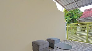 Un petit espace extérieur aménagé avec deux poufs gris et une table ronde, le tout posé sur un sol carrelé.