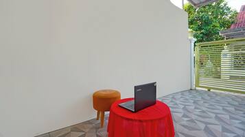 A room with a red table and a laptop, a tiled floor, and a green gate in the background.