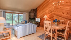 A cozy, log-furnished room with a fireplace, a dining table with chairs, and a striped sofa. - Pet Friendly, Single Level Condo Across from Clubhouse (Sunriver)