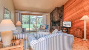 A cozy living room with striped sofas, a fireplace, and a sign reading "Sunset Lodging." - Pet Friendly, Single Level Condo Across from Clubhouse (Sunriver)