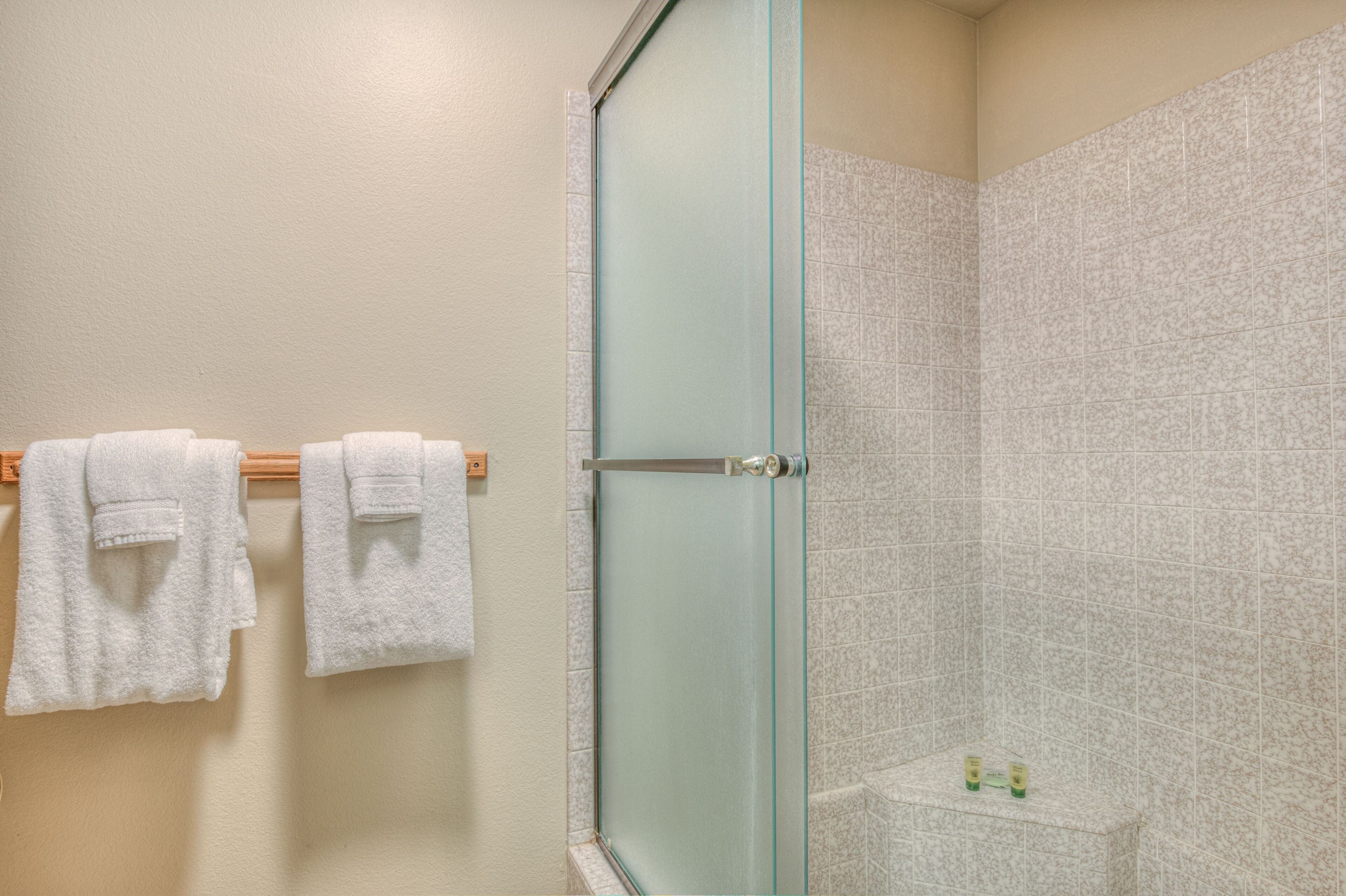 A bathroom with a glass shower door, white towels on a rack, and a small shelf with toiletries.