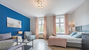 A modern bedroom with a bed, bedside table, lamp, and a view of the outdoors through large windows. - Apartament Przytulny na Starym Mieście 2 sypialnie (Gdansk)