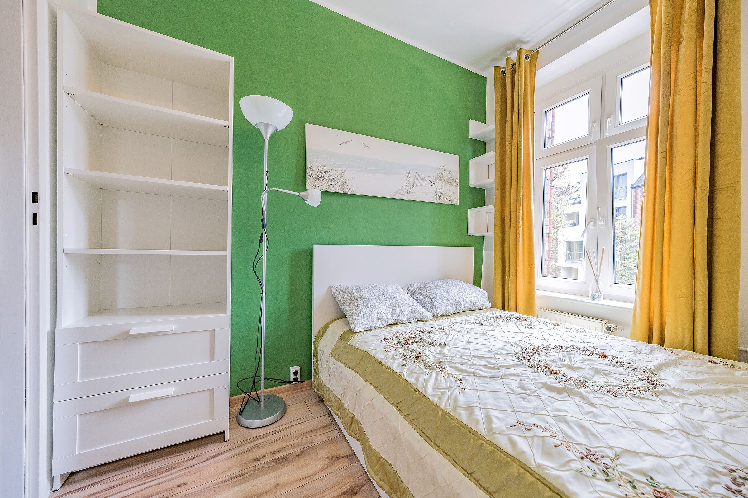 Un dormitorio con cama, un armario blanco, una lámpara de pie y una ventana con cortinas amarillas.