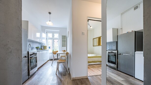 A modern kitchen with stainless steel appliances, a wooden dining table, and a view of the city through the window. - Apartament Przytulny na Starym Mieście 2 sypialnie (Gdansk)